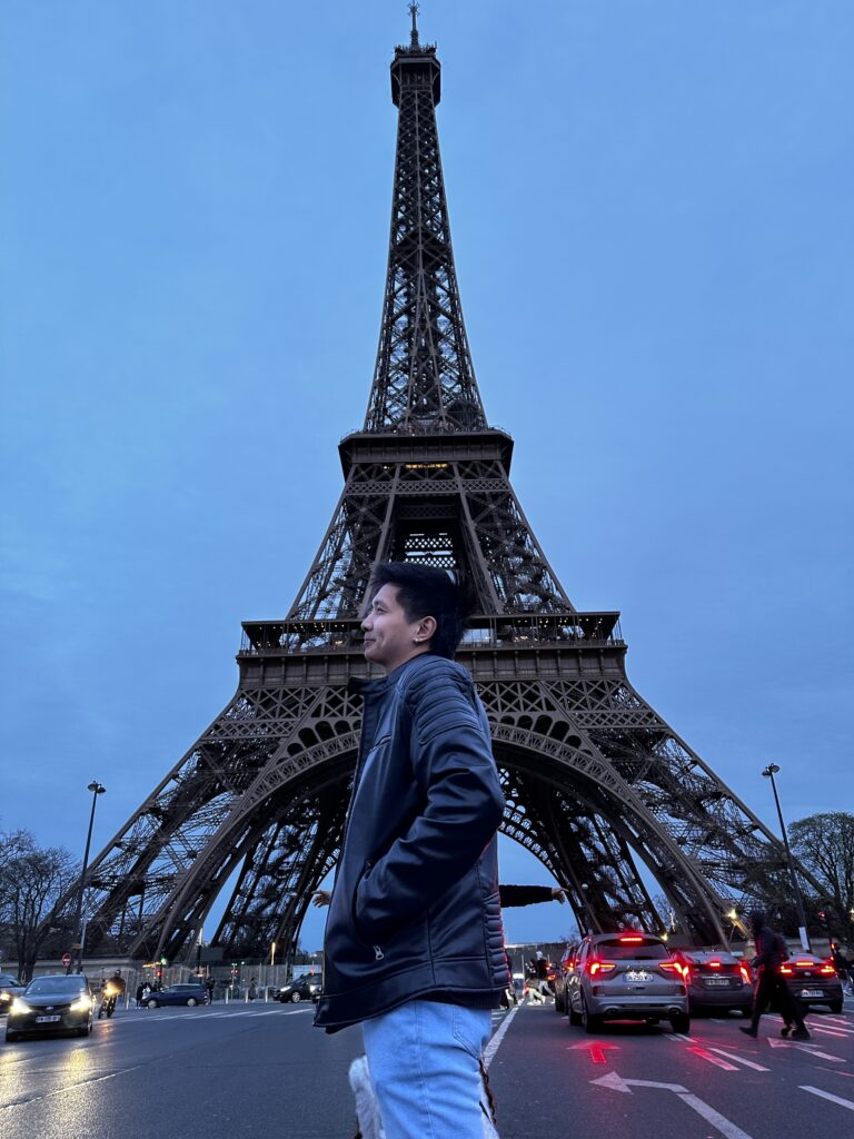 Man wearing jacket standing behind the paris eiffel tower during sunset